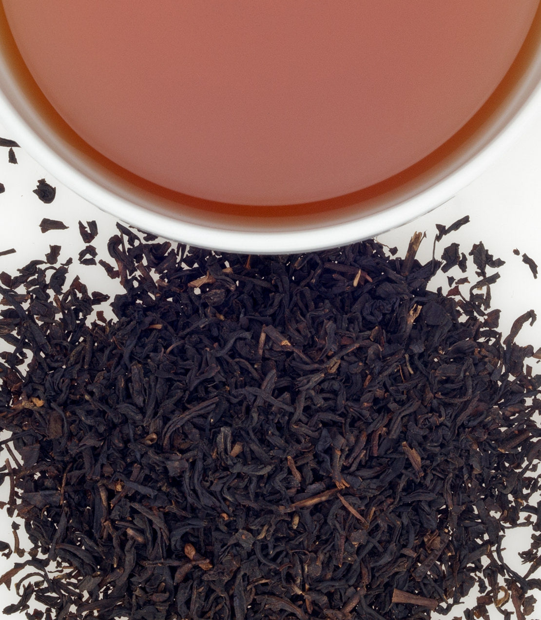 A close-up of loose black tea leaves beside a cup of brewed tea, showcasing rich color and texture.