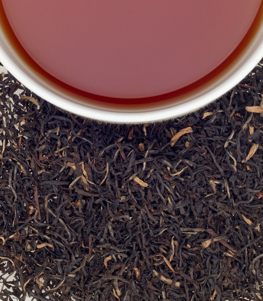 A close-up of Brigitte's Blend tea, featuring a cup of brewed tea above loose black tea leaves.
