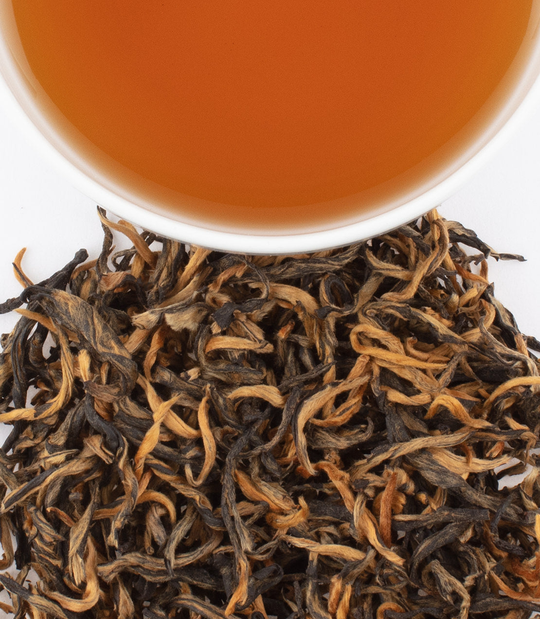 A close-up of Canton Honey Black tea leaves beside a cup of brewed tea, showcasing rich amber color and texture.