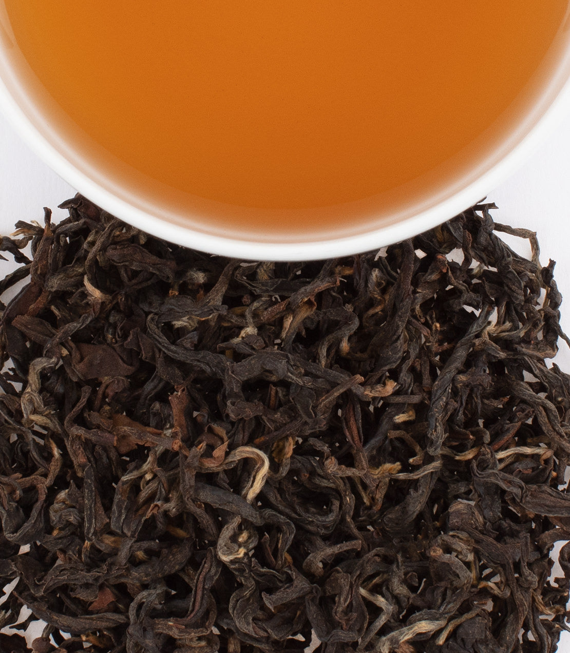 Ceylon Golden Curl tea leaves with brewed tea in a white cup, showcasing rich color and texture.