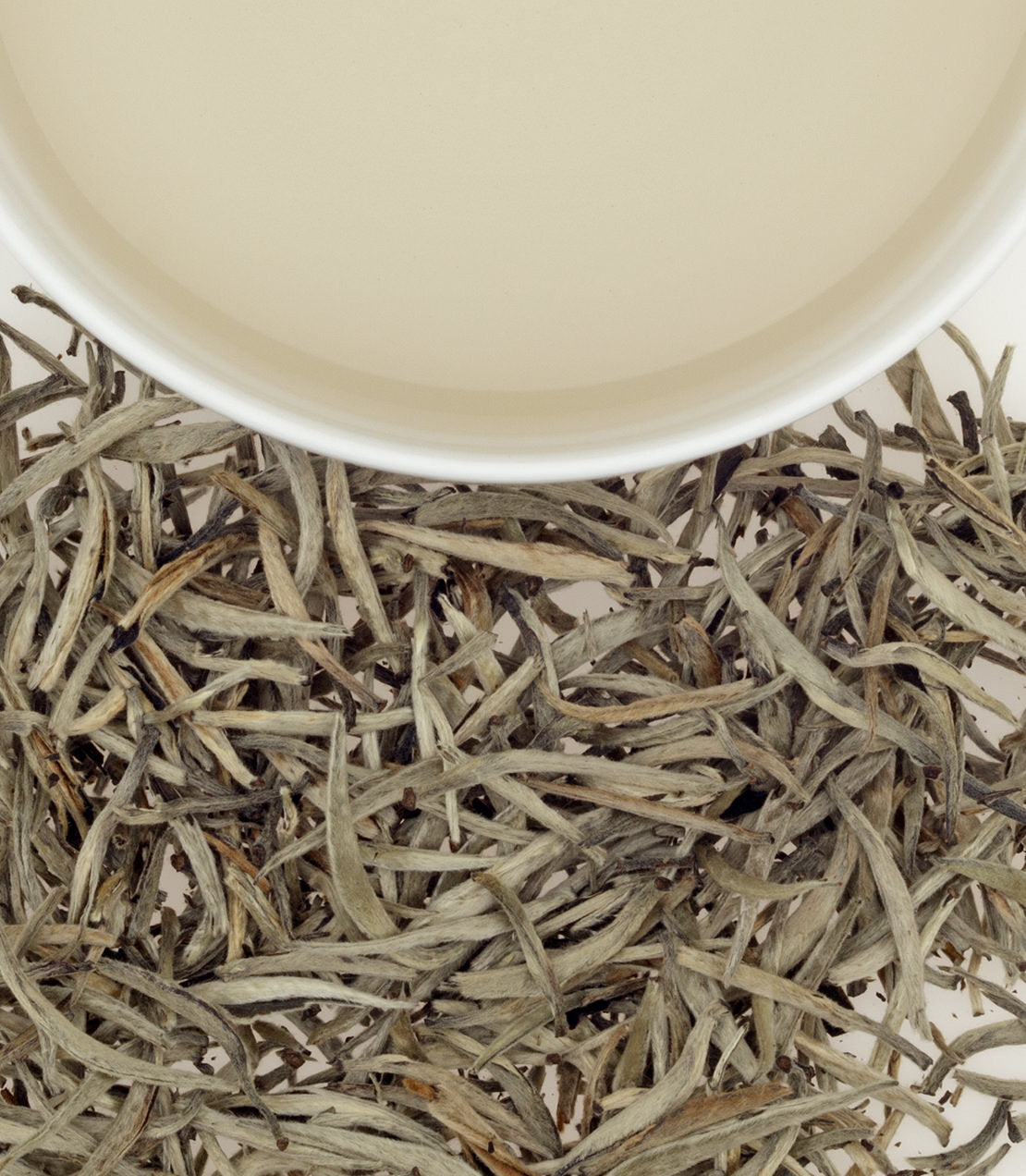 Ceylon Vintage Silver Tips tea leaves beside a cup of pale, brewed tea, showcasing their delicate appearance.