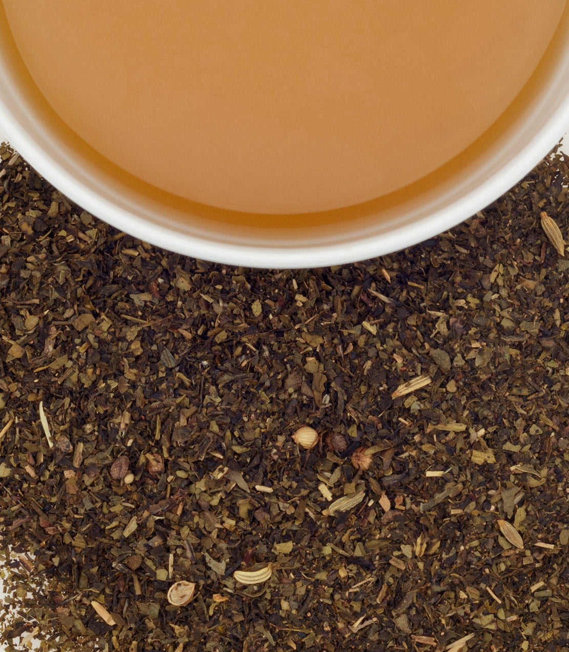 A cup of brewed green chai surrounded by loose tea leaves and spices, showcasing its rich color and texture.