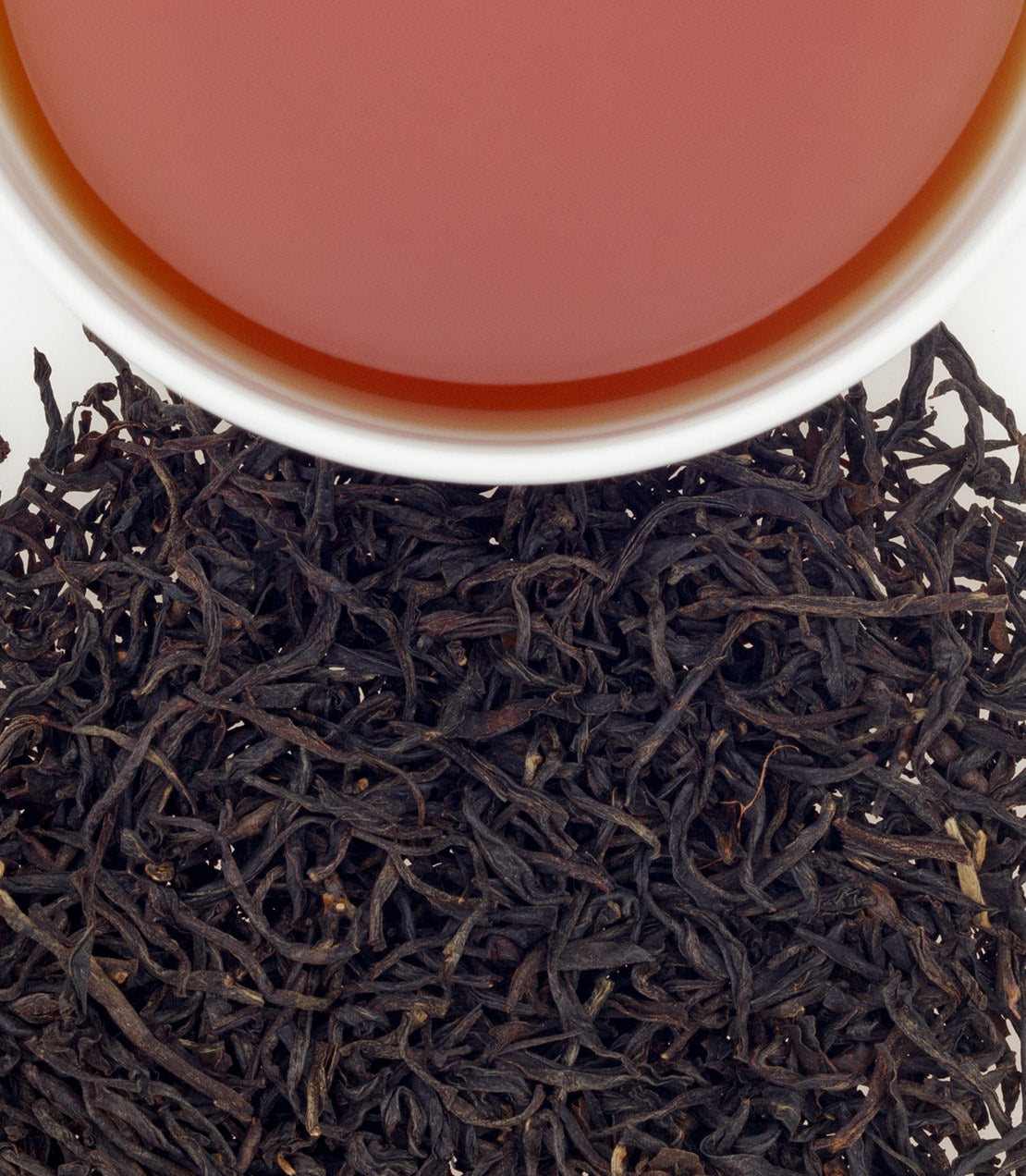 A cup of Colombian black tea above a bed of loose, dark tea leaves, showcasing rich color and texture.