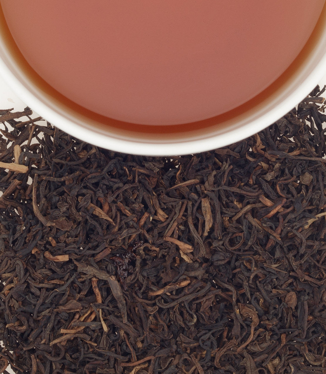 A cup of decaf apricot tea above loose black tea leaves, showcasing a warm, amber hue.