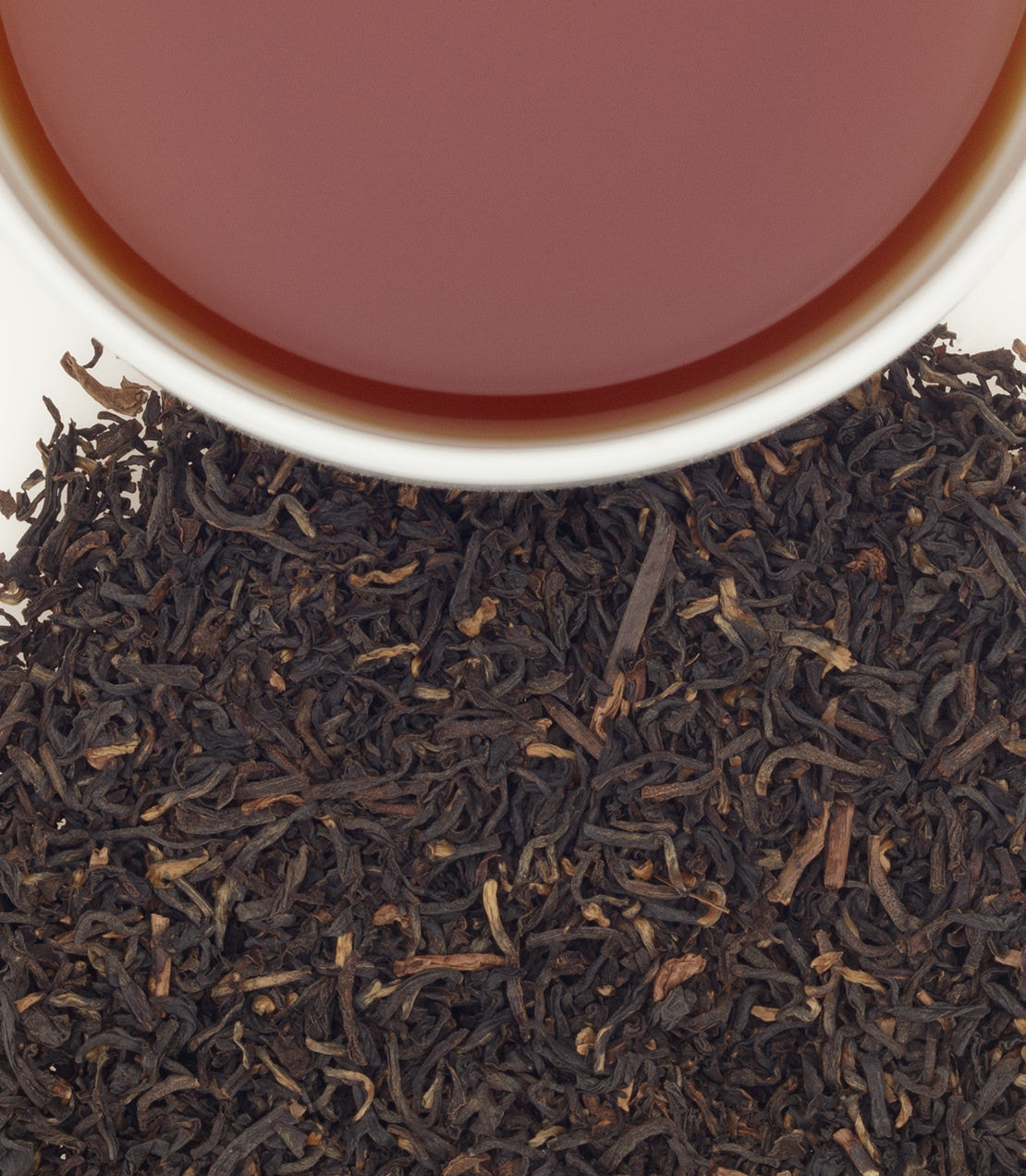 A cup of brewed decaf Assam tea above loose black tea leaves, showcasing rich color and texture.