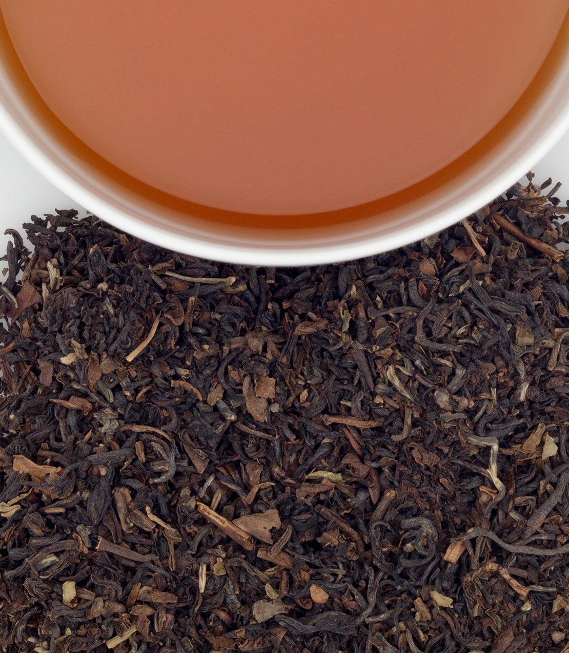 Decaf Darjeeling tea leaves with brewed tea in a white cup, showcasing rich color and texture.