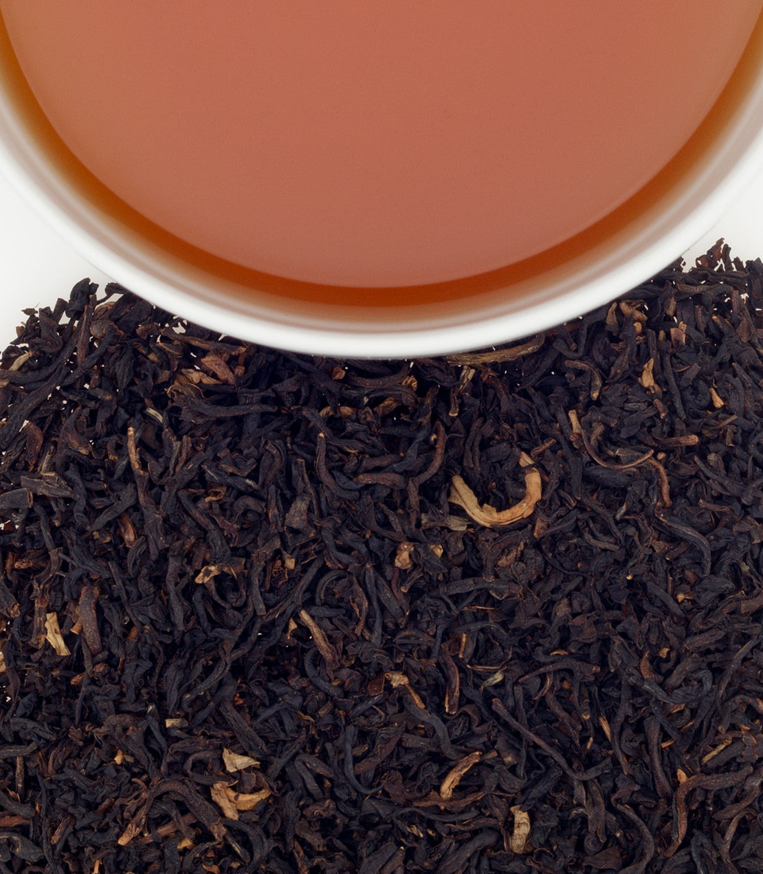 A cup of decaf mango tea above loose black tea leaves, showcasing a warm, inviting color.