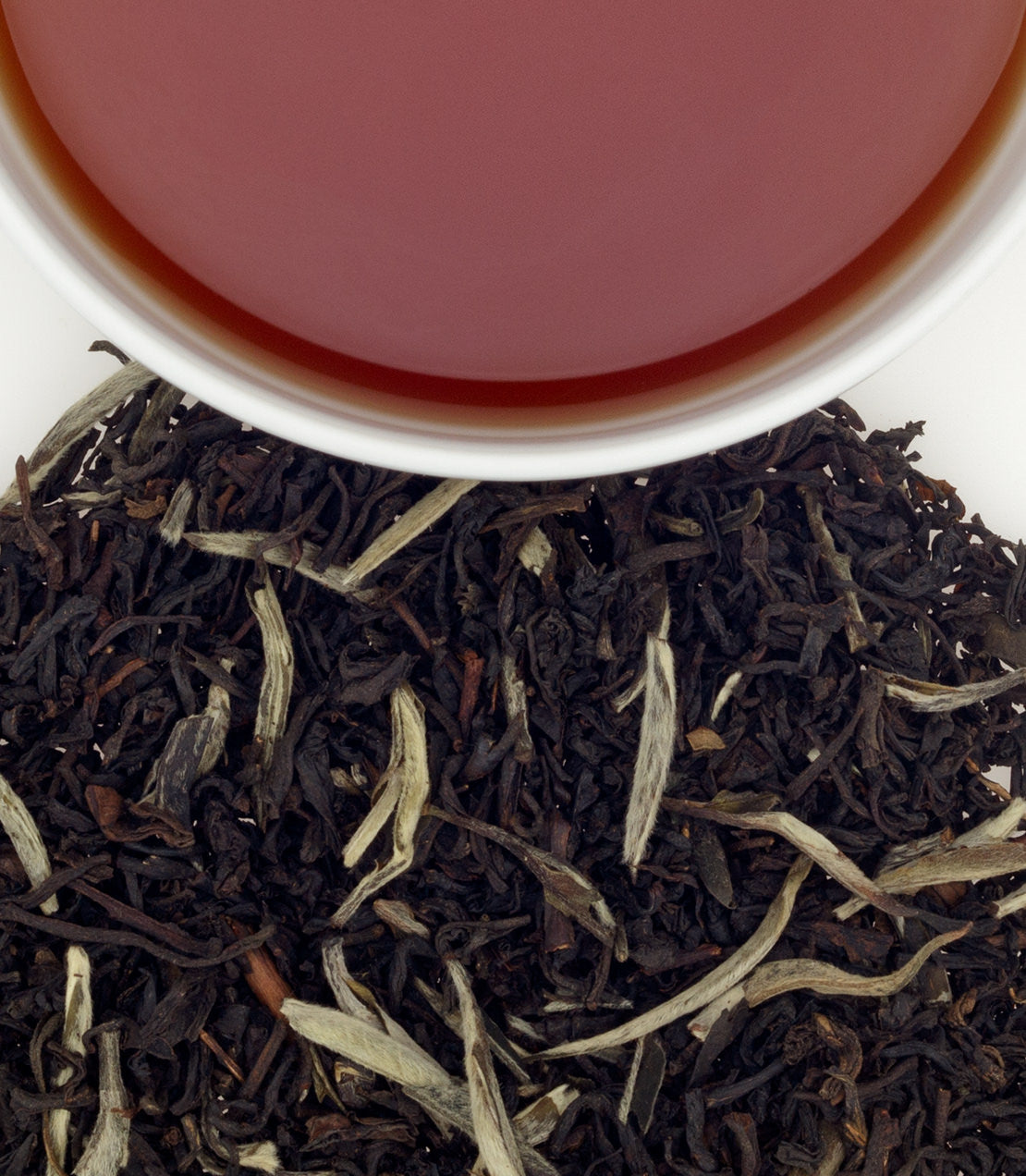 A close-up of loose black tea leaves with a cup of brewed tea above, showcasing rich color and texture.