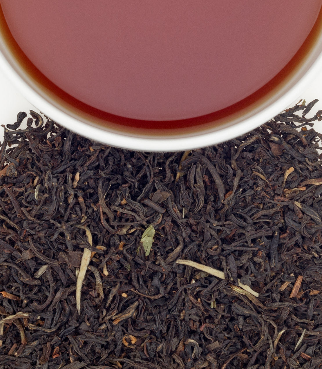 A close-up of a cup of brewed tea above loose black tea leaves, showcasing rich color and texture.