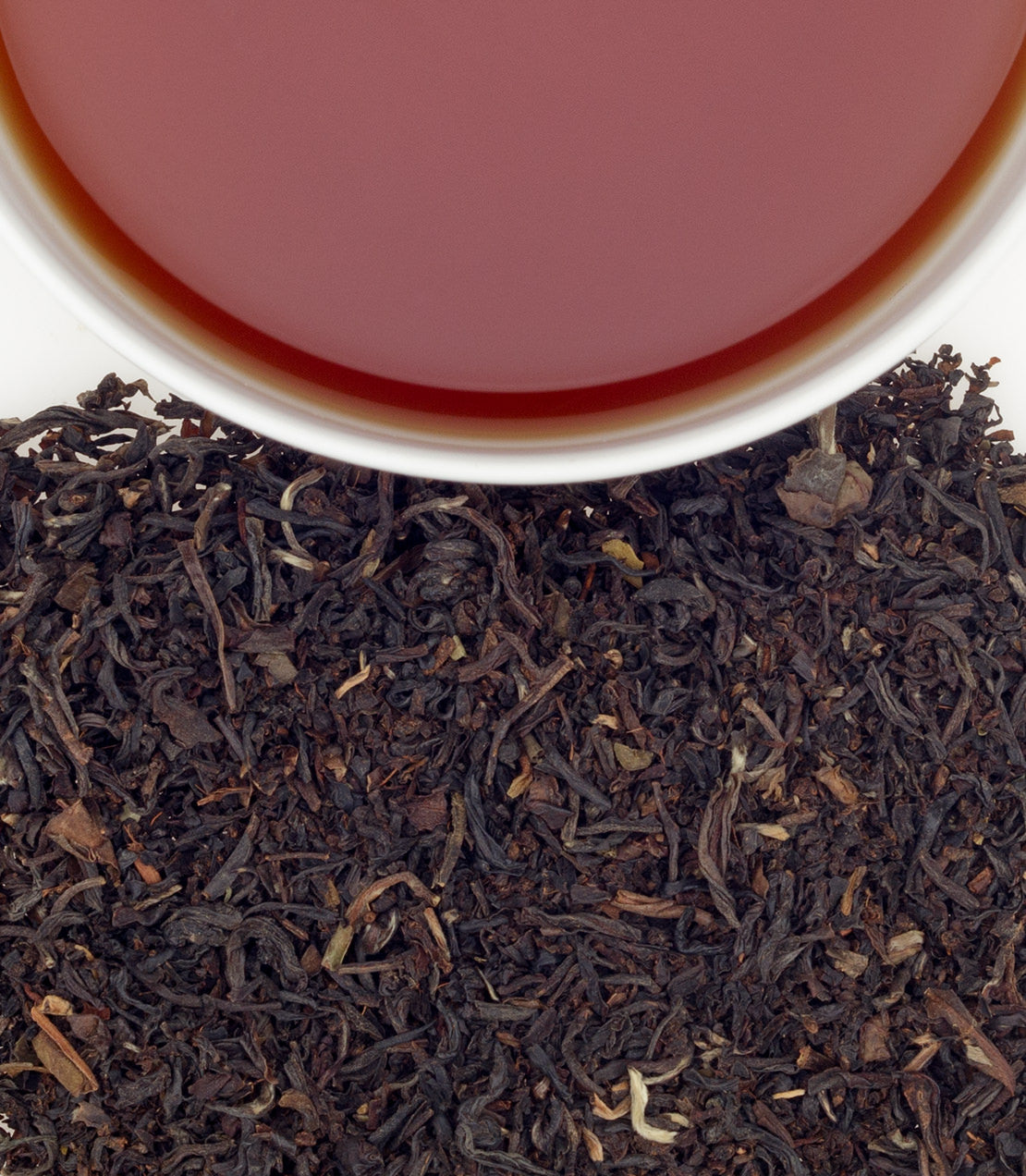A close-up of Elaine's Blend tea leaves with a cup of brewed tea above, showcasing rich colors and textures.