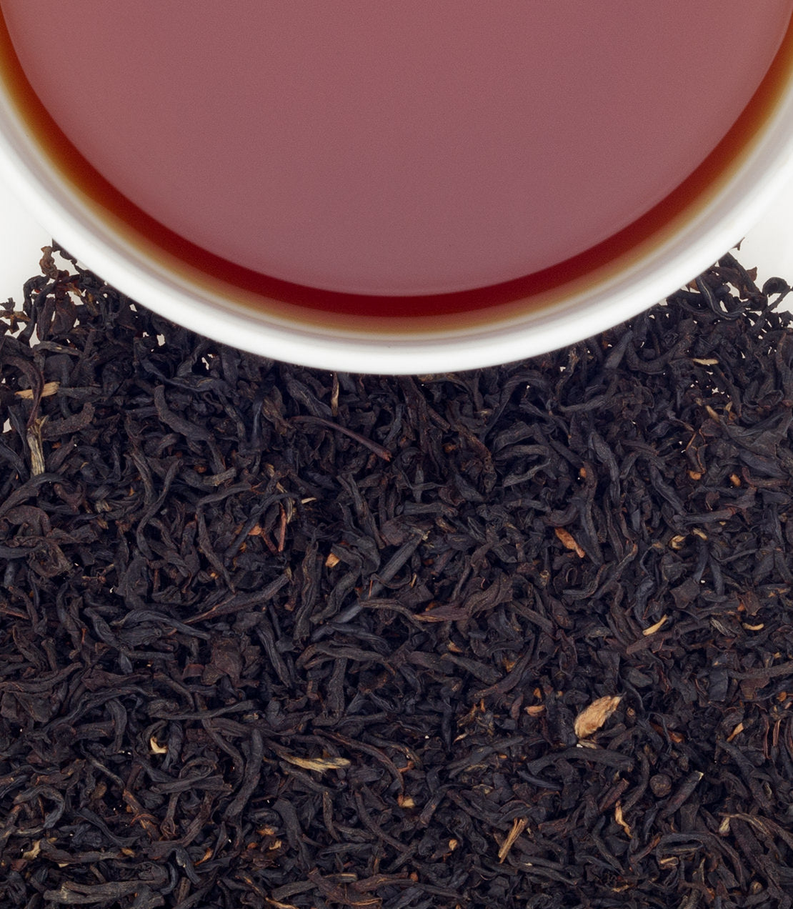 A cup of brewed Elyse's Blend tea sits atop loose black tea leaves, showcasing rich color and texture.