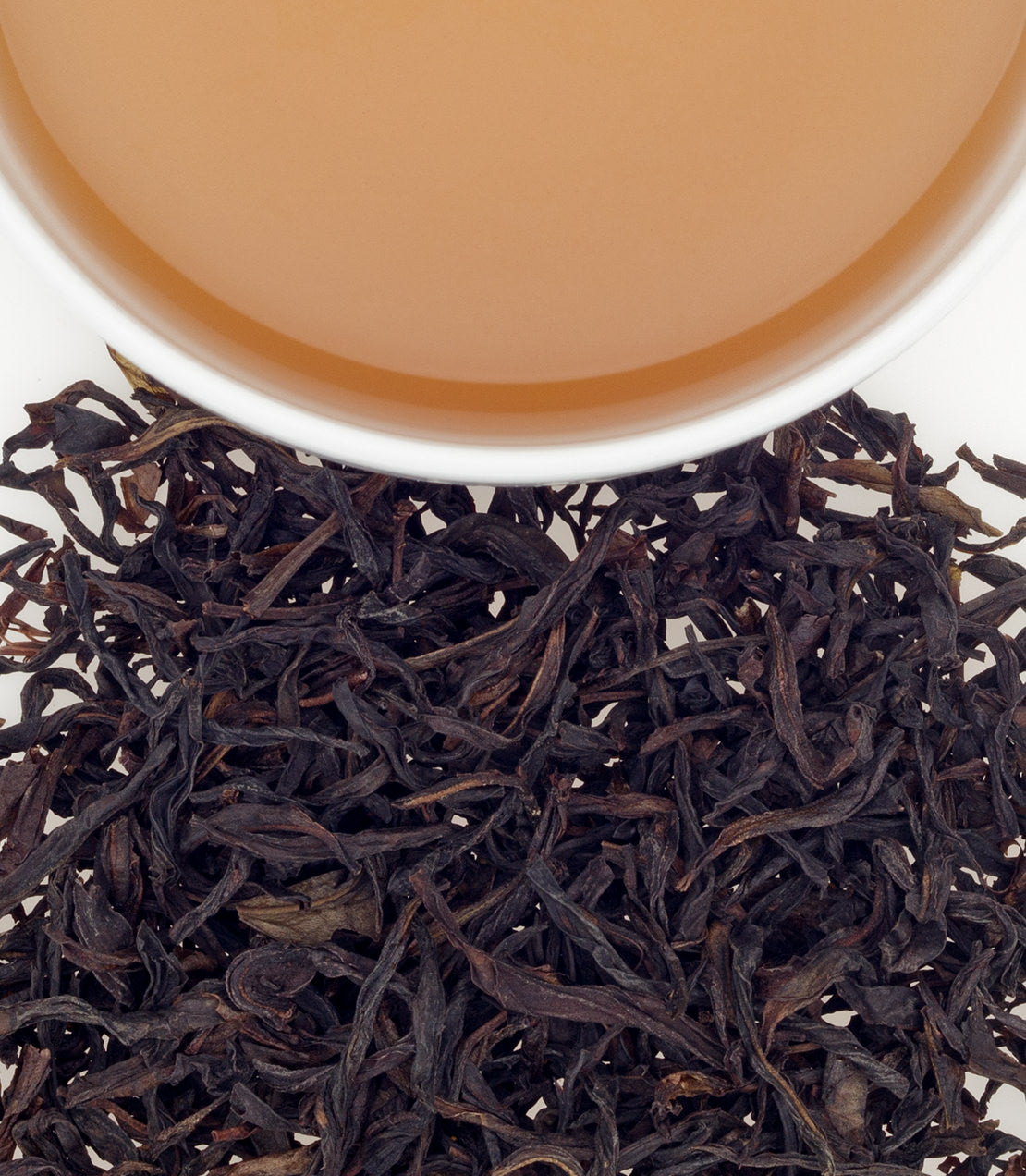 Fenghuang Shuixian tea leaves with brewed tea in a white cup, showcasing rich color and texture.
