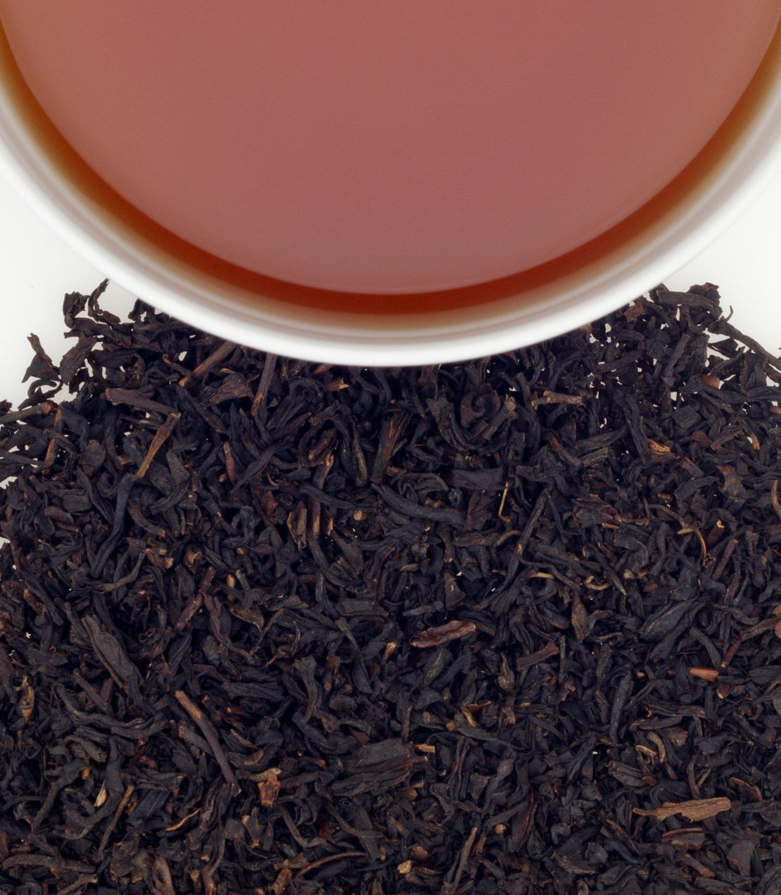 A close-up of a cup of brewed tea above a pile of loose black tea leaves, showcasing rich color and texture.