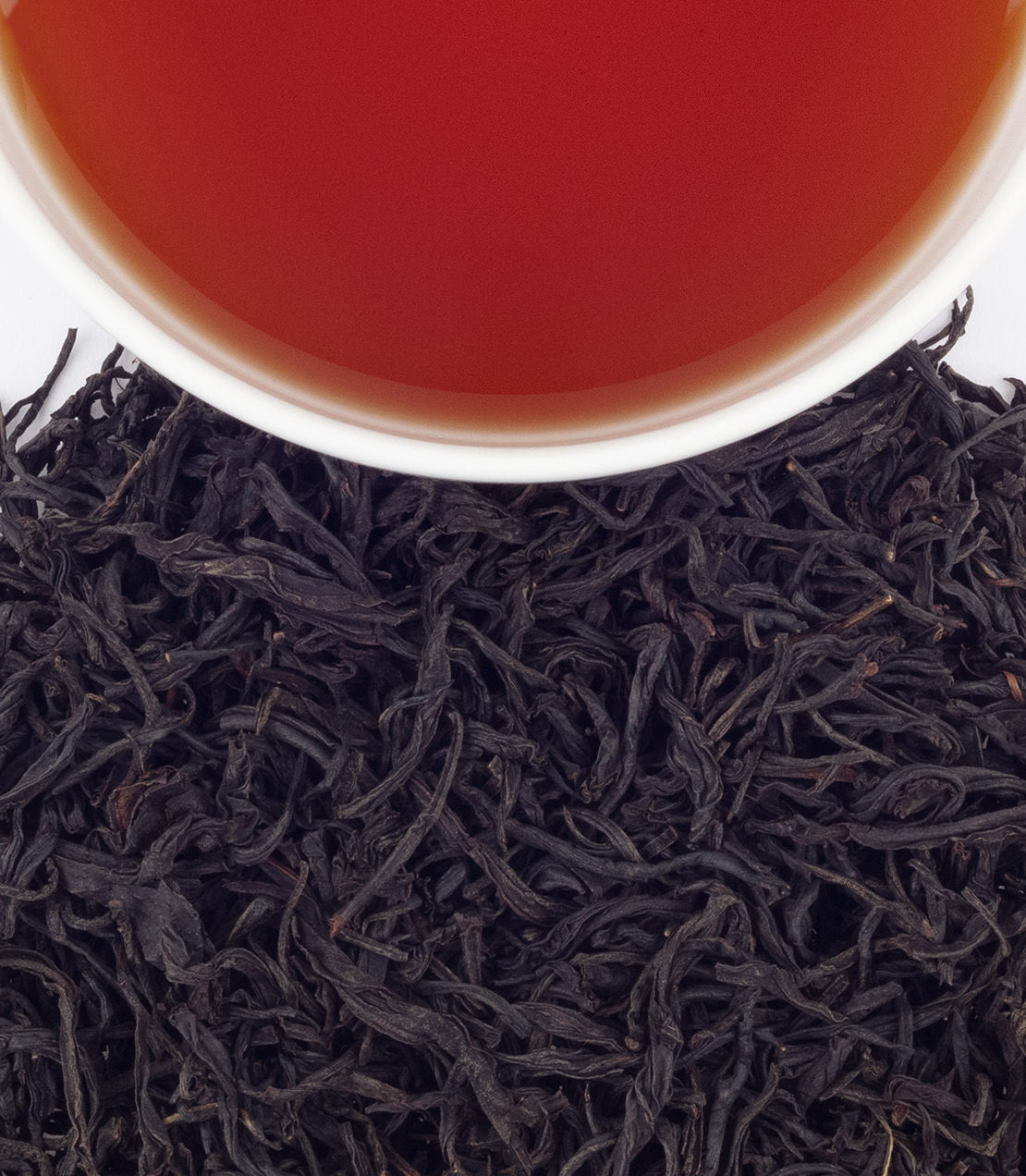 A cup of Ruby Black tea above a bed of loose black tea leaves, showcasing rich color and texture.