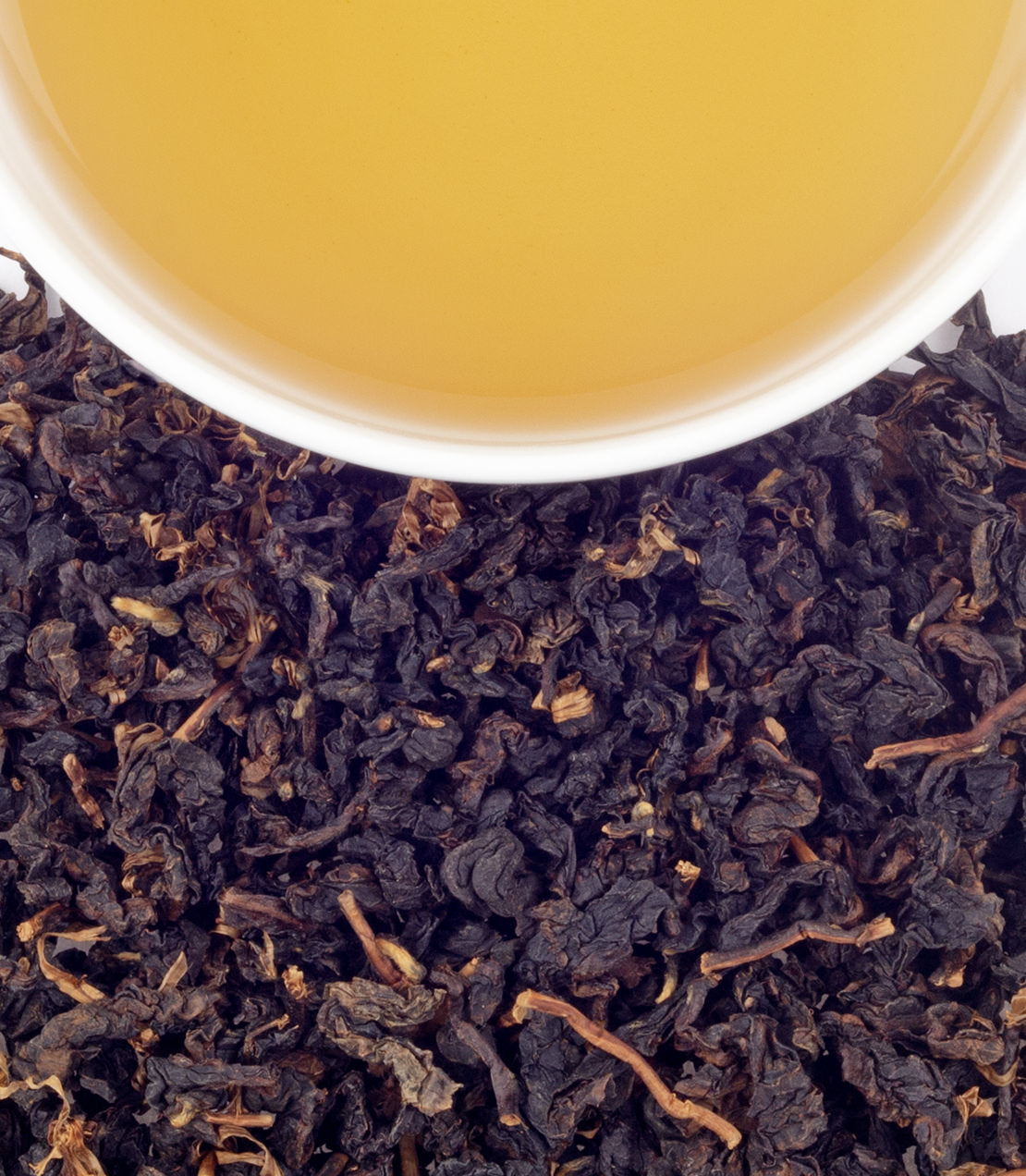 A cup of Gaba Oolong tea above dried, dark oolong tea leaves, showcasing its rich color and texture.