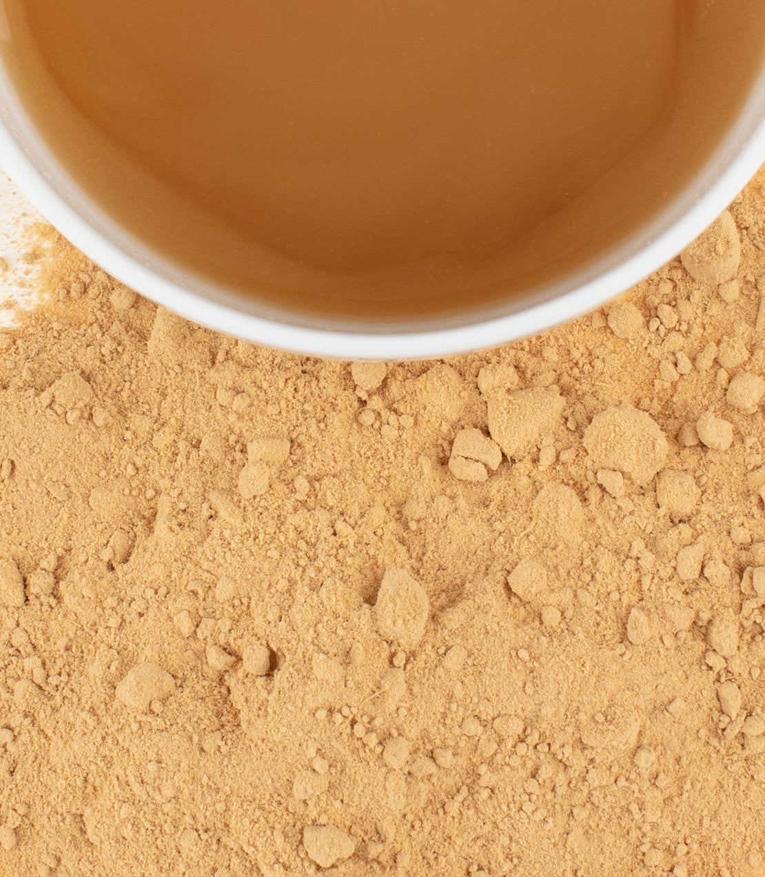 Organic ginger powder scattered on a surface, with a cup of ginger tea in the background.
