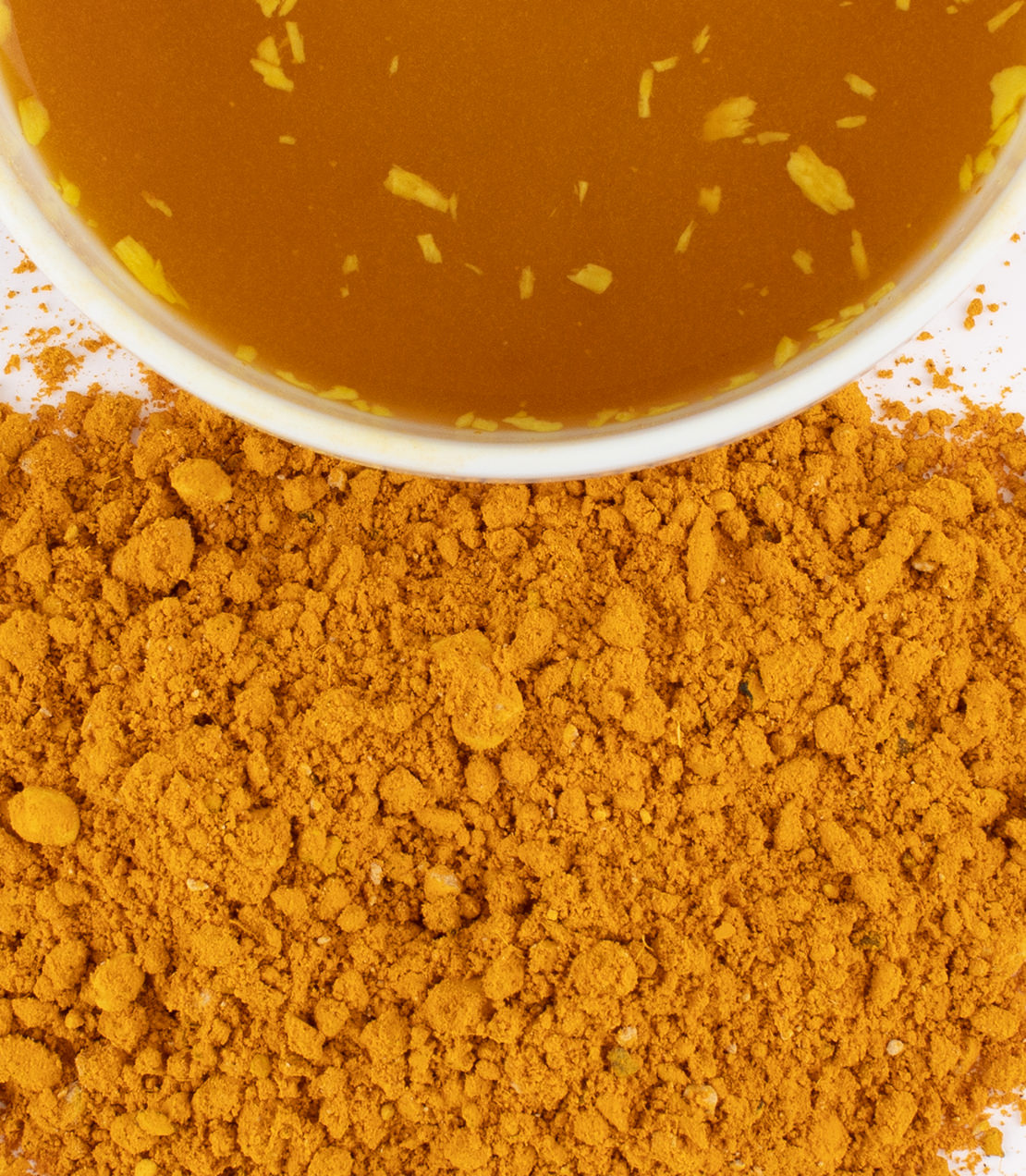 A bowl of organic golden milk next to a mound of golden turmeric powder, showcasing the Glimmer Wellness Blend.