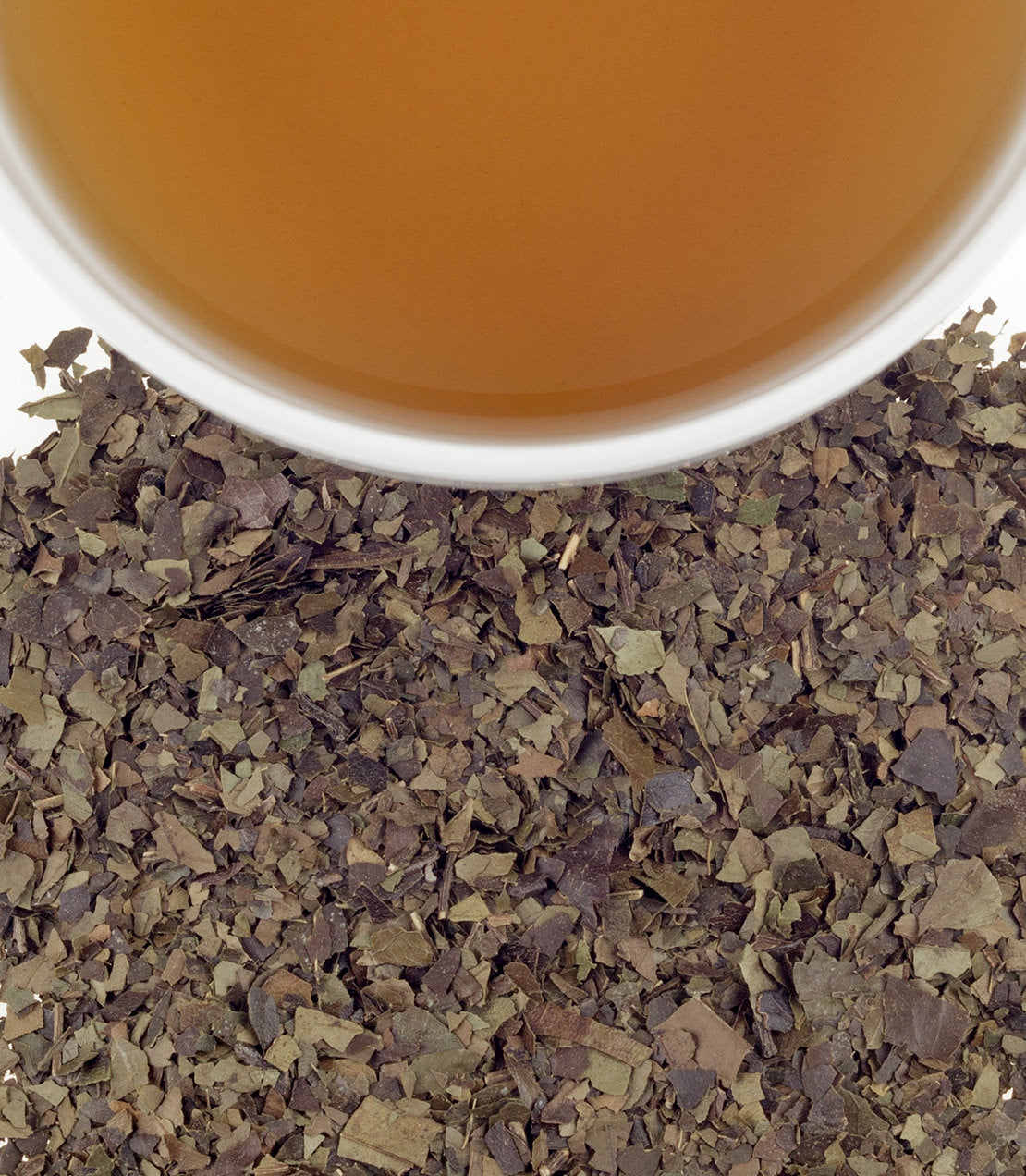 A cup of brewed guayusa tea above loose guayusa leaves, showcasing its earthy color and texture.