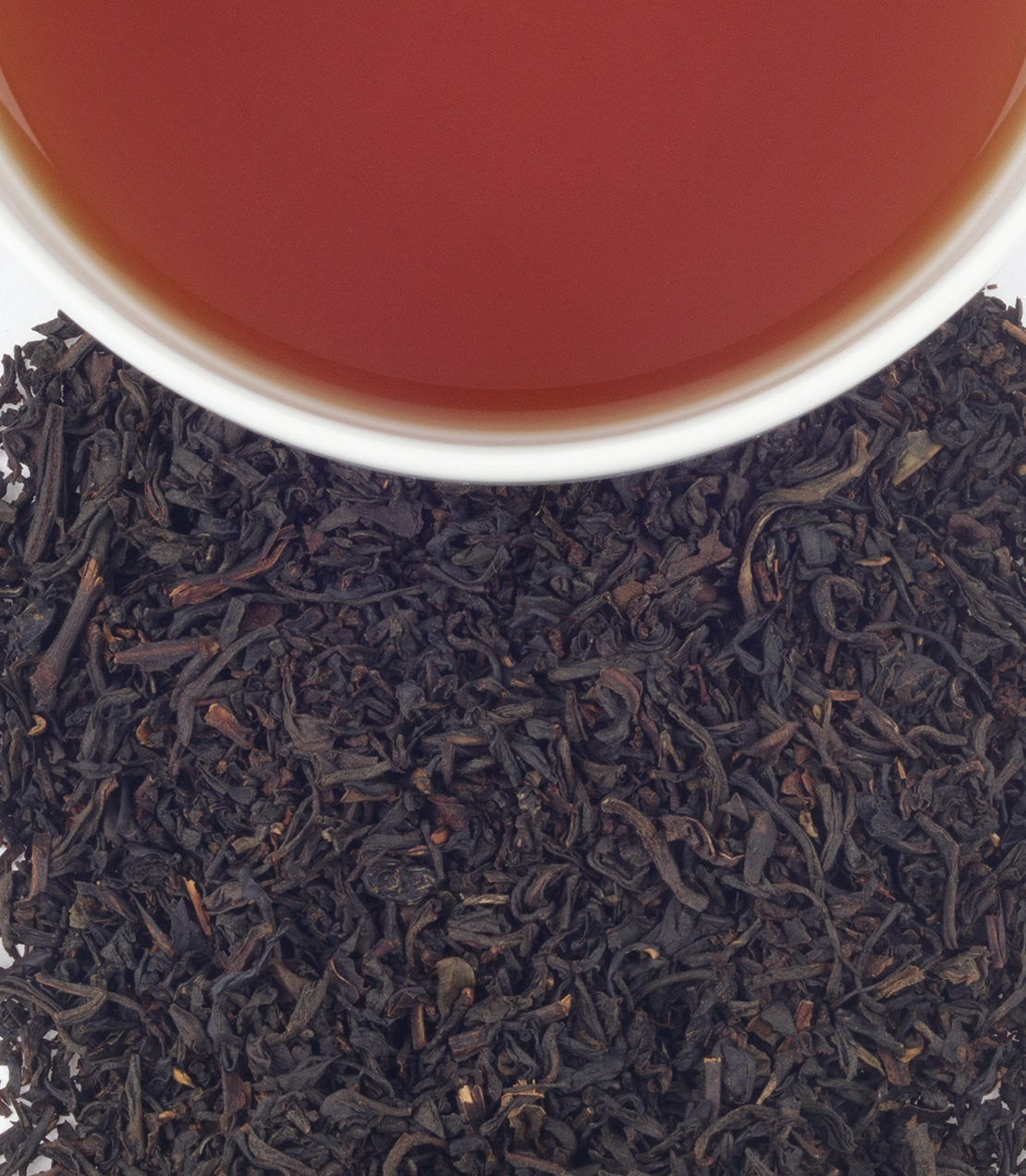 A close-up of loose black tea leaves with a cup of brewed tea above, showcasing rich color and texture.