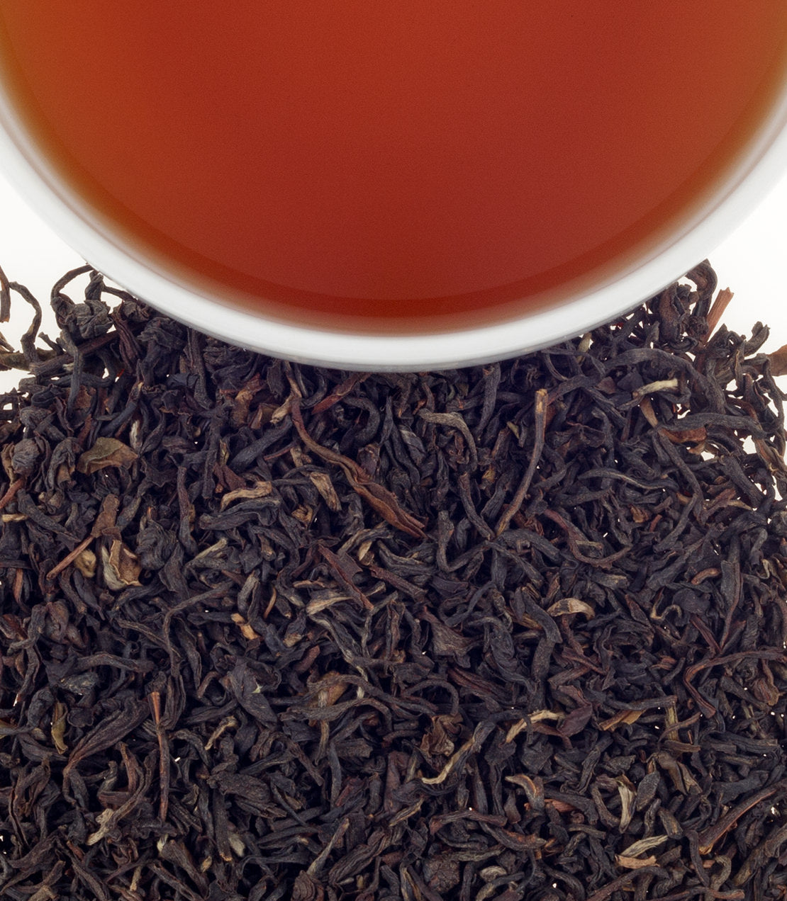 A close-up of loose black tea leaves with a cup of brewed tea above, showcasing rich color and texture.