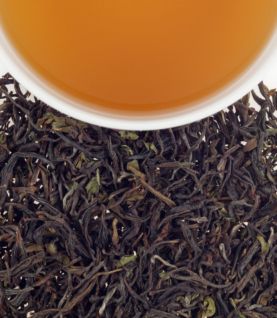 A cup of Havakai Frost Tea above loose black tea leaves, showcasing its rich amber color and texture.