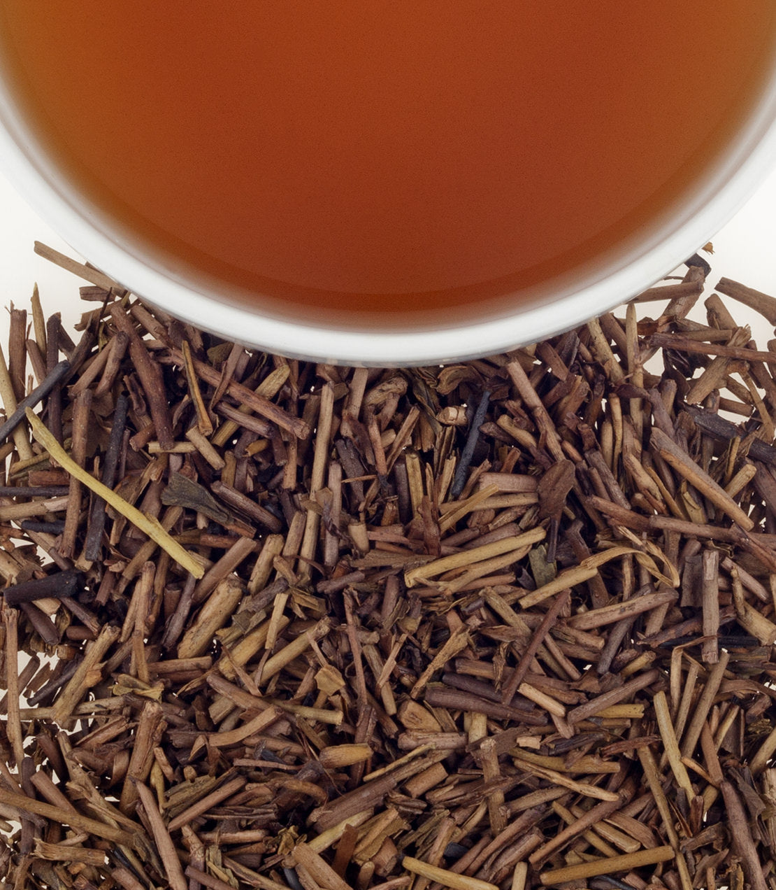 A cup of brewed hojicha tea above roasted tea leaves, showcasing the rich brown color and unique texture.