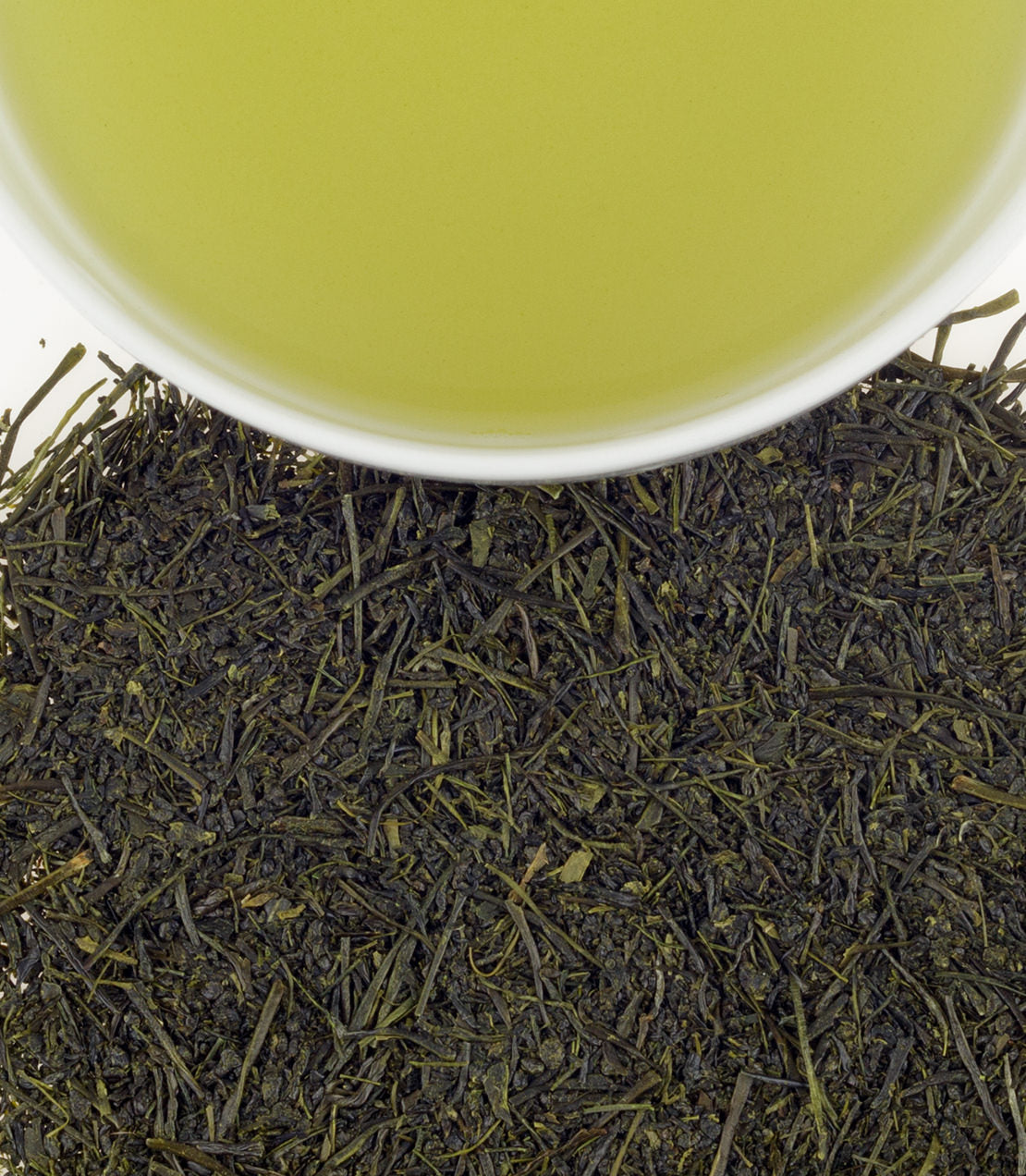 Freshly brewed Ichiban Sencha green tea in a white cup above loose tea leaves, showcasing vibrant green hues.