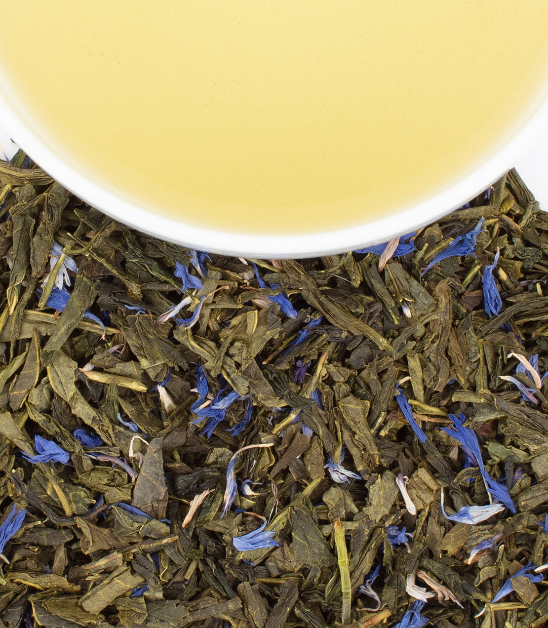 A close-up of green tea leaves with blue flower petals, next to a cup of light yellow tea.