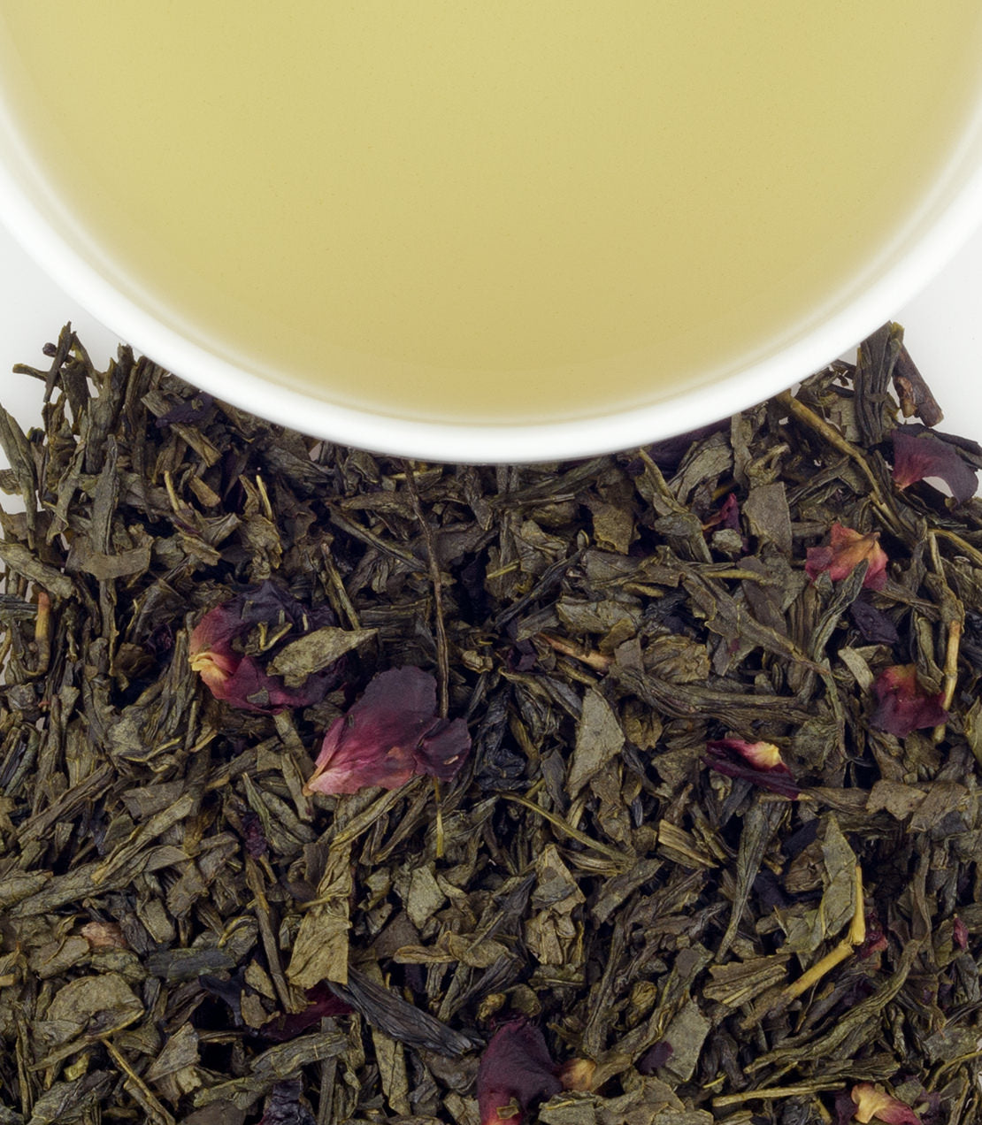 A cup of Jane's Garden Tea above loose green tea leaves and dried rose petals, showcasing its delicate color and texture.