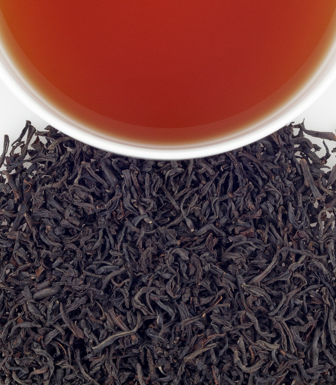 A close-up of Kenilworth Ceylon tea leaves with a cup of brewed tea above, showcasing rich color and texture.