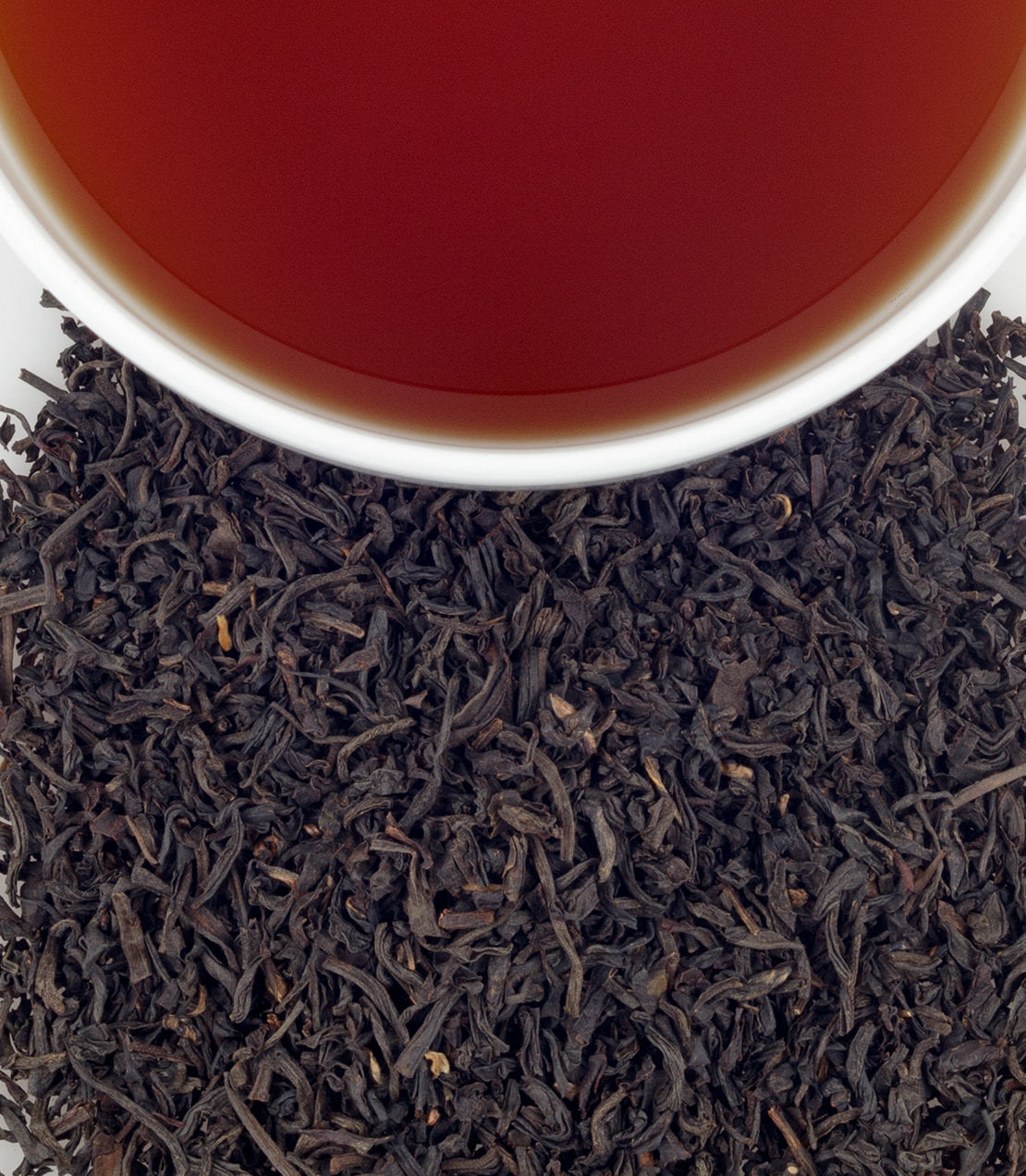 A close-up of loose black tea leaves with a cup of brewed tea above, showcasing rich amber color.