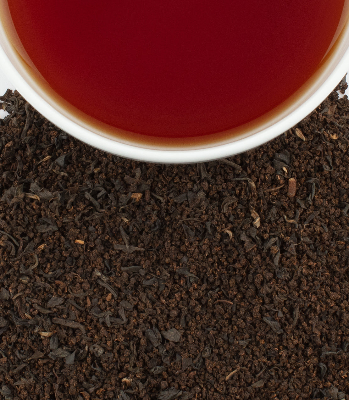 A close-up of a cup of brewed Mayfair Breakfast tea above loose black tea leaves, showcasing rich color and texture.