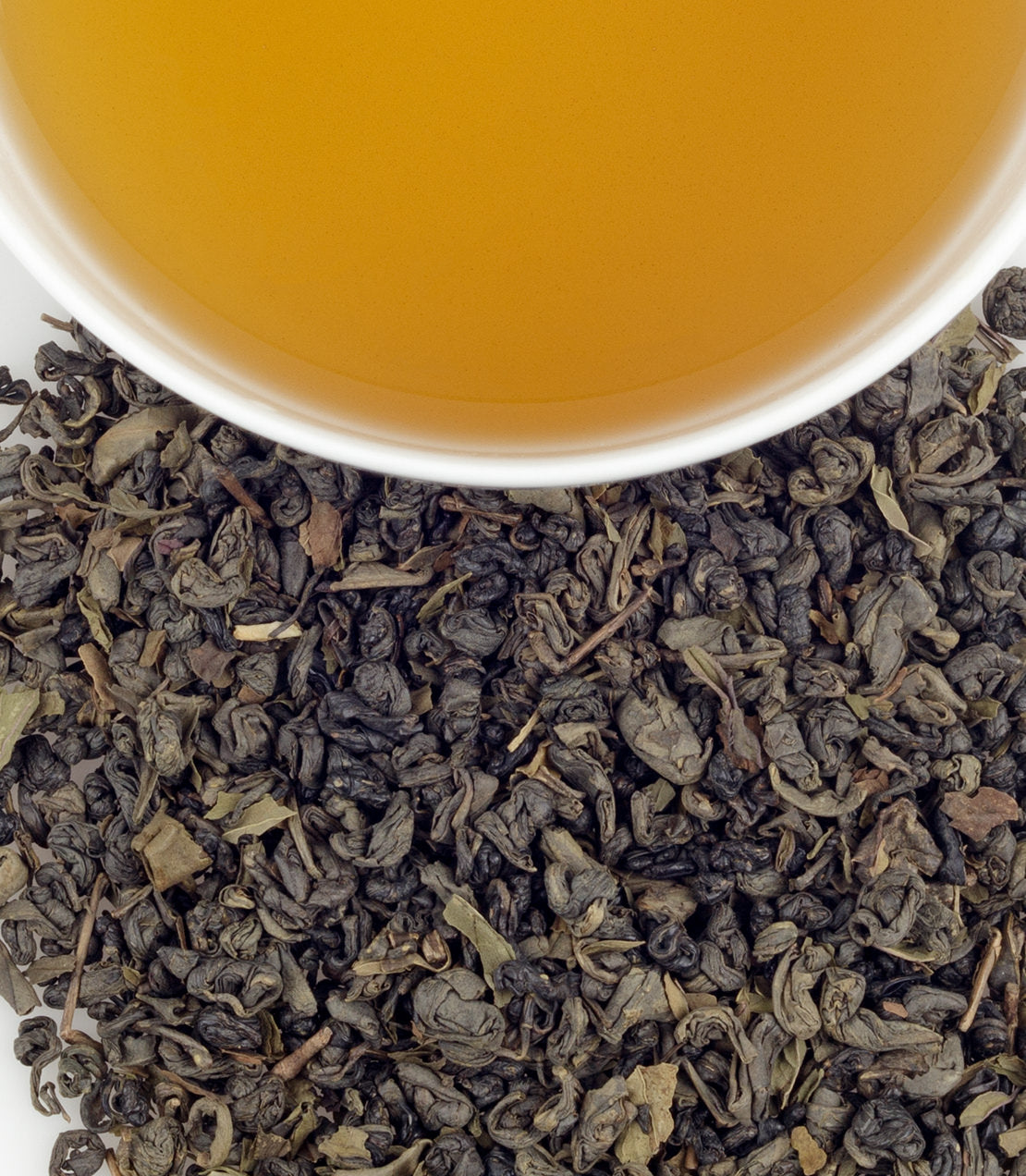 Organic Moroccan Mint tea leaves scattered around a cup of brewed tea, showcasing rich color and aroma.