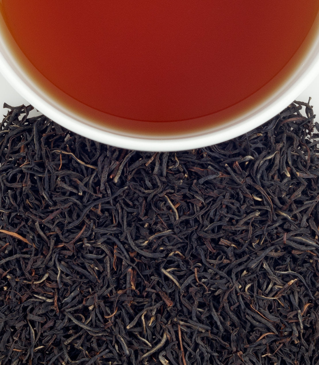 A close-up of loose black tea leaves with a cup of brewed tea, showcasing the rich color and texture of Vithanakande tea.