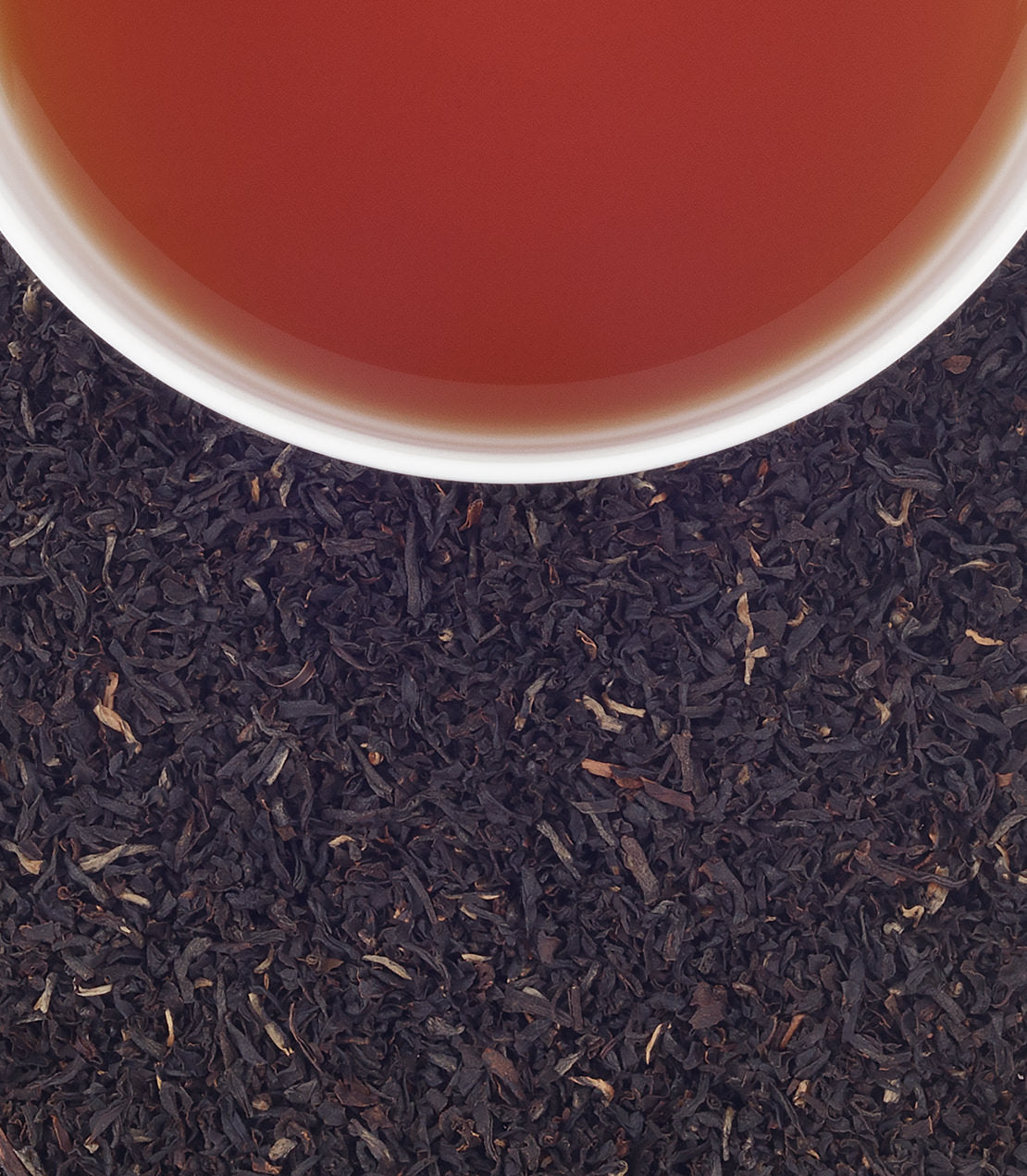 A cup of brewed organic Assam tea above loose black tea leaves, showcasing rich color and texture.