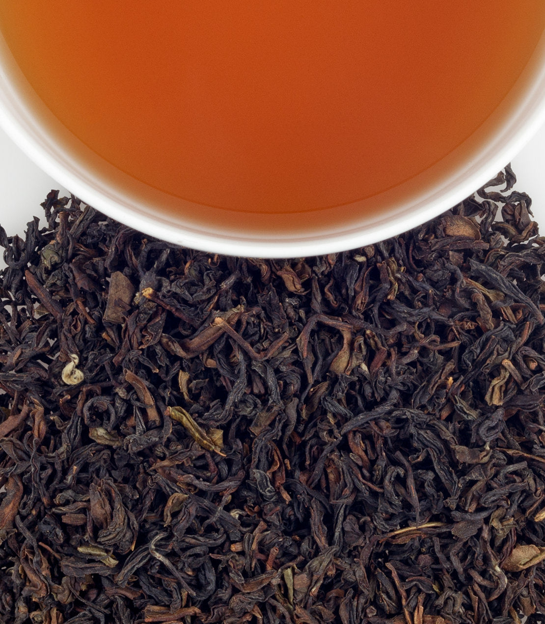 Organic Darjeeling tea leaves with brewed tea in a white cup, showcasing rich color and texture.