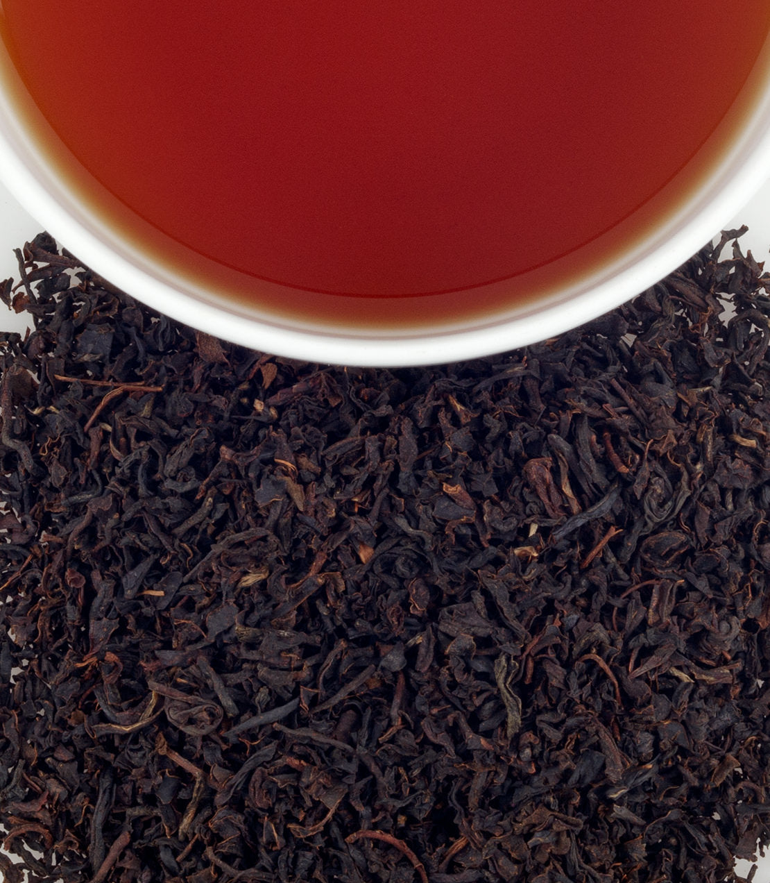 A cup of brewed organic Earl Grey tea above loose black tea leaves, showcasing rich color and texture.