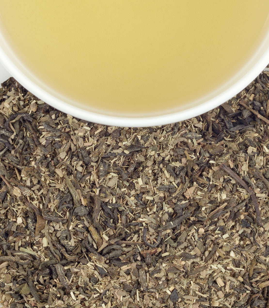 Cup of organic green tea with citrus and ginkgo, surrounded by loose tea leaves on a textured surface.
