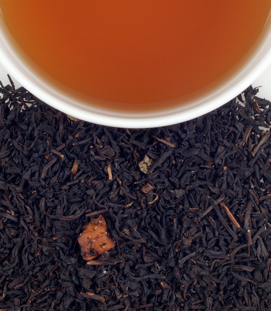 A cup of brewed Peaches & Ginger tea above loose black tea leaves, showcasing a sachet of the blend.