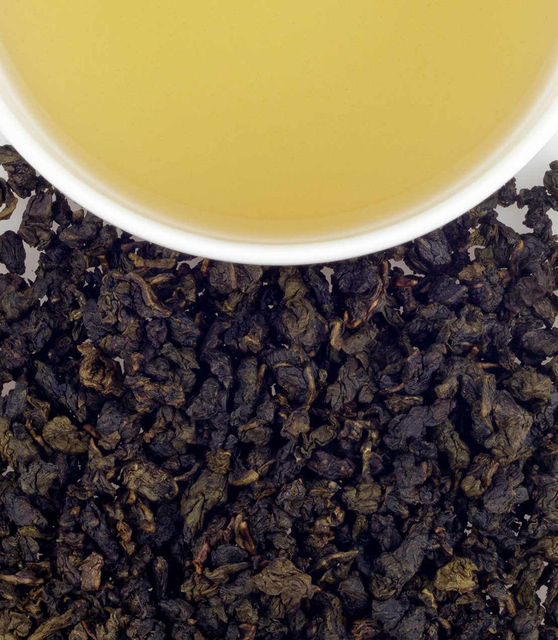 Pomegranate Oolong tea in a cup above loose tea leaves, showcasing a vibrant yellow brew and rich texture.