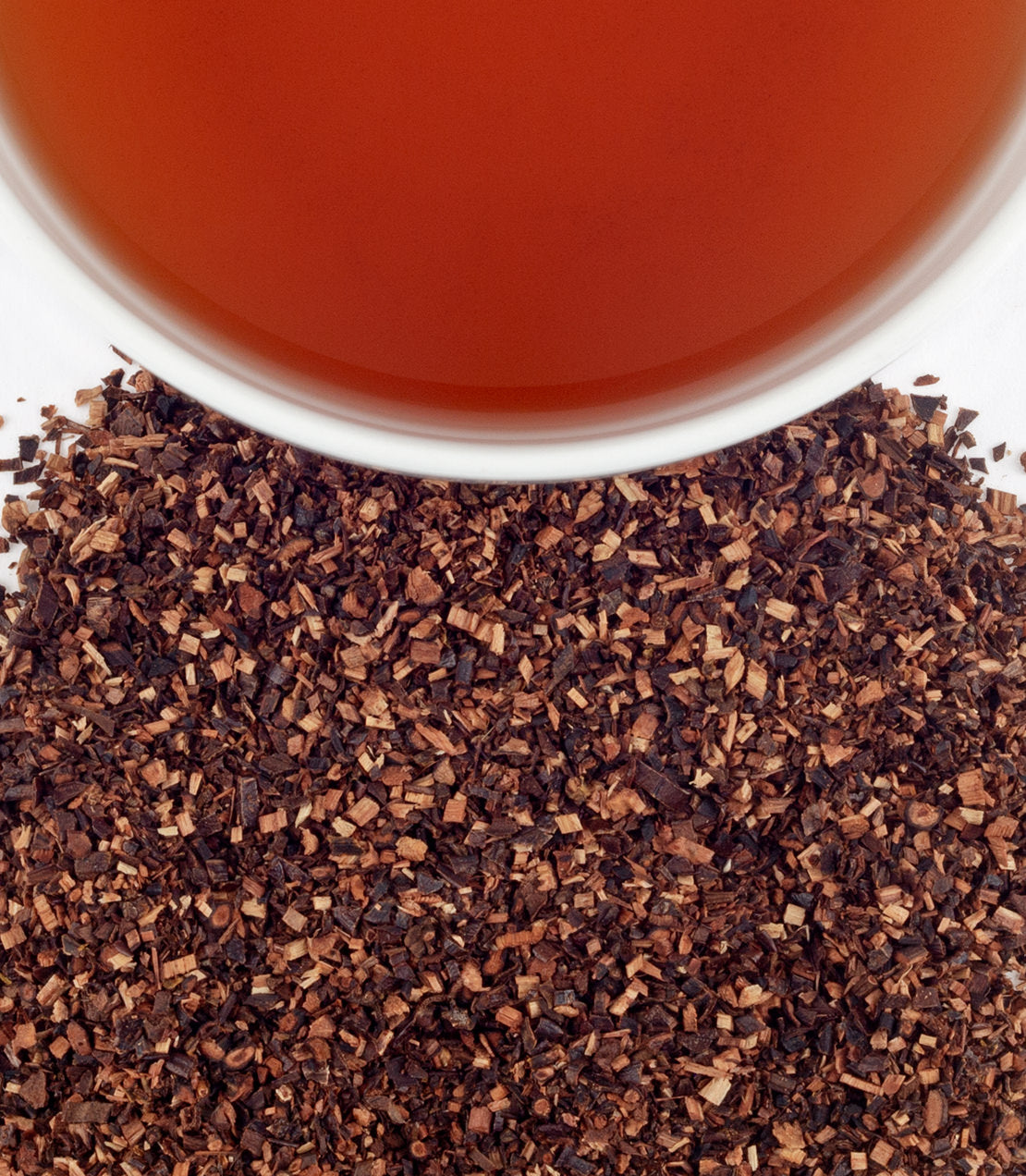 Pure Wild Honeybush tea with loose leaves scattered around a cup of brewed tea. Rich amber color.