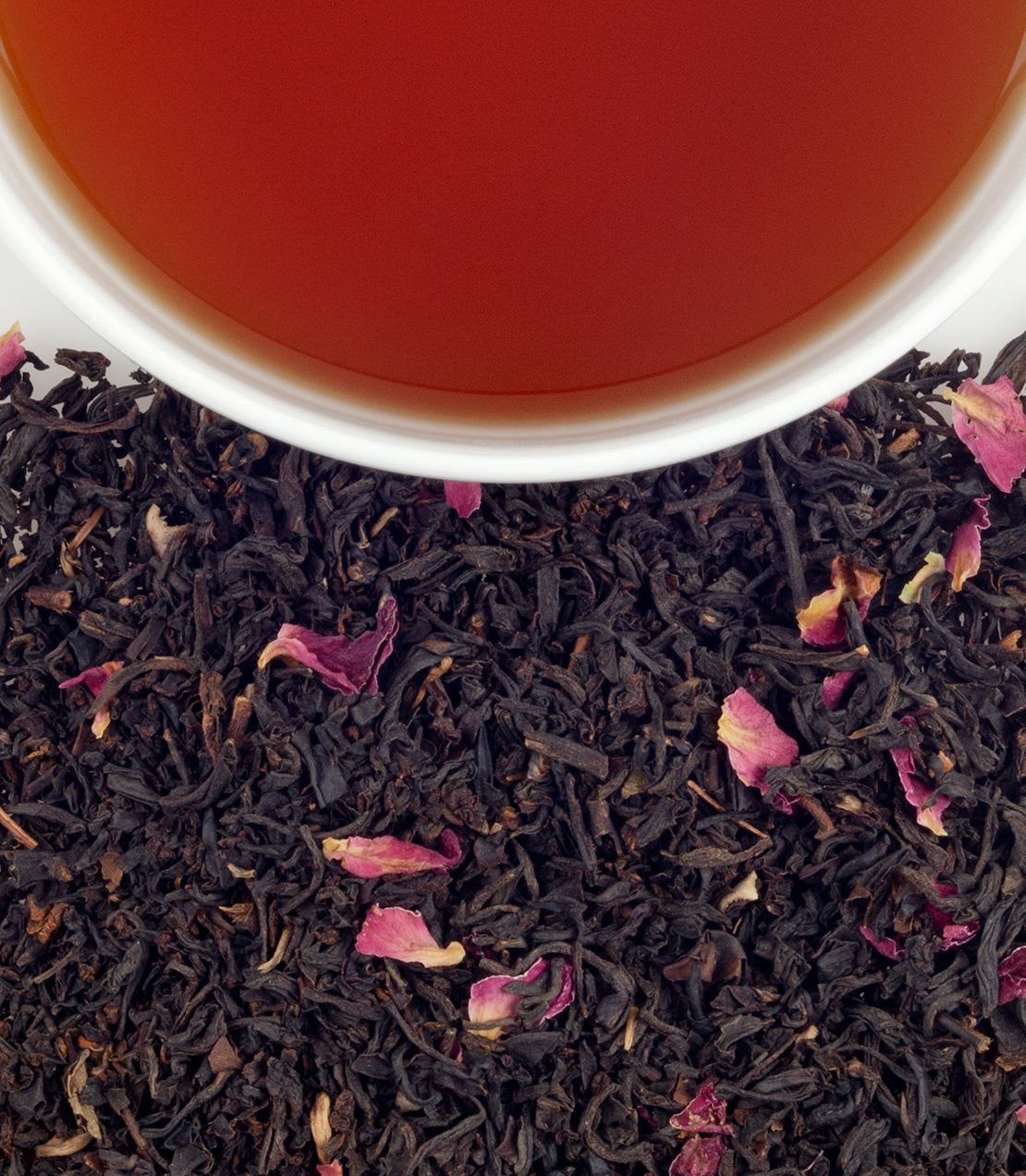 A close-up of loose black tea leaves with dried rose petals, alongside a cup of brewed tea.