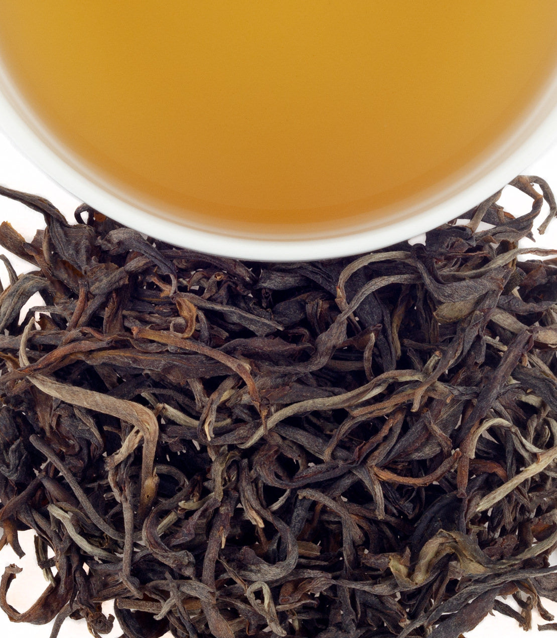 A cup of brewed Thai silk tea above loose dried tea leaves, showcasing its rich color and texture.