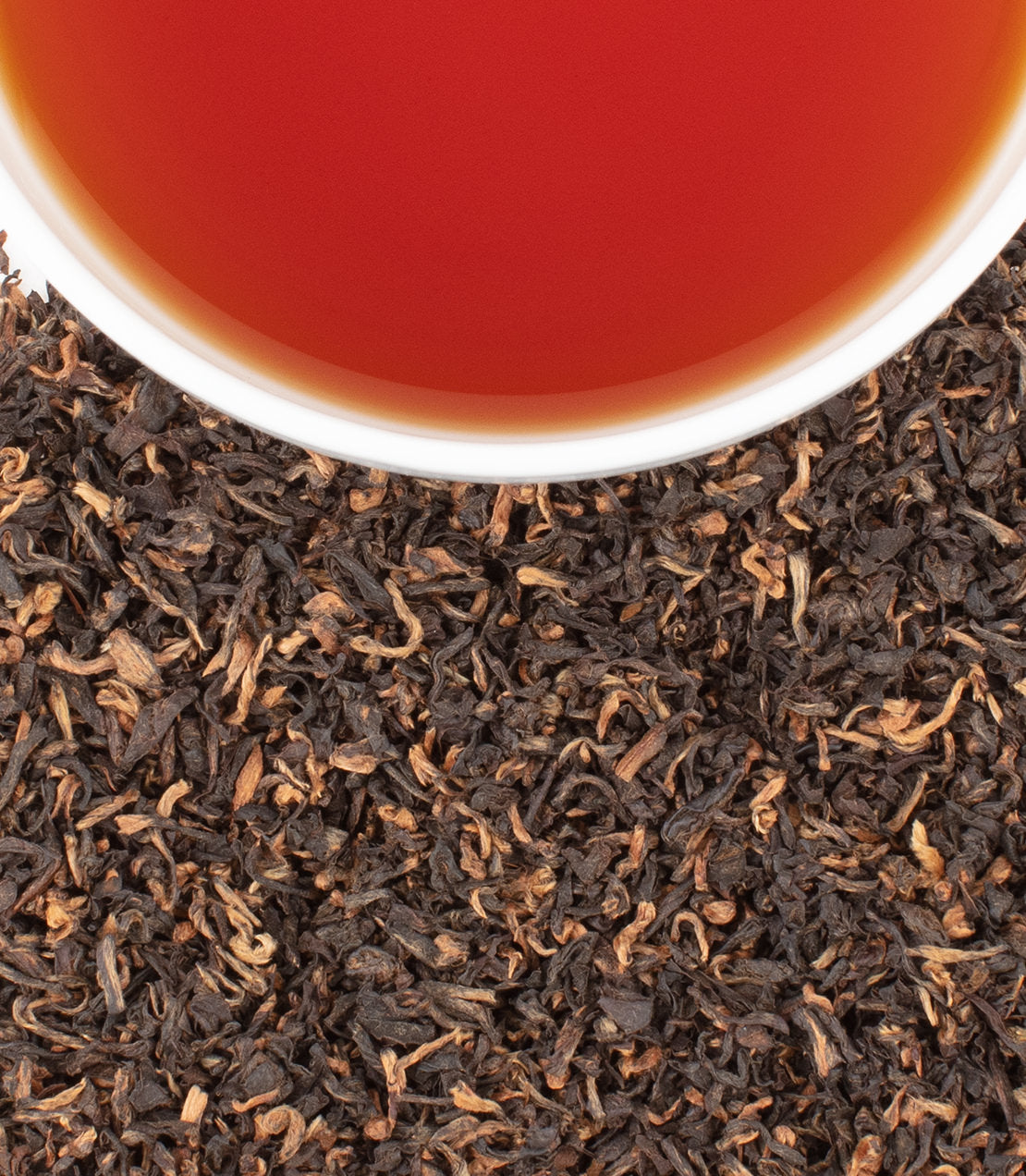 Halmari Broken Assam tea leaves with a cup of brewed tea, showcasing rich color and texture.