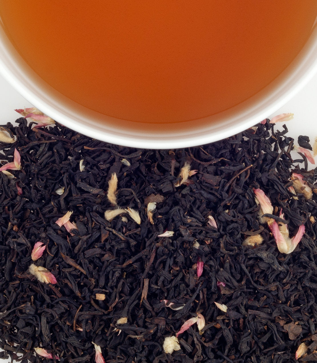 SoHo Blend tea with loose black tea leaves and rose petals beside a cup of brewed tea.