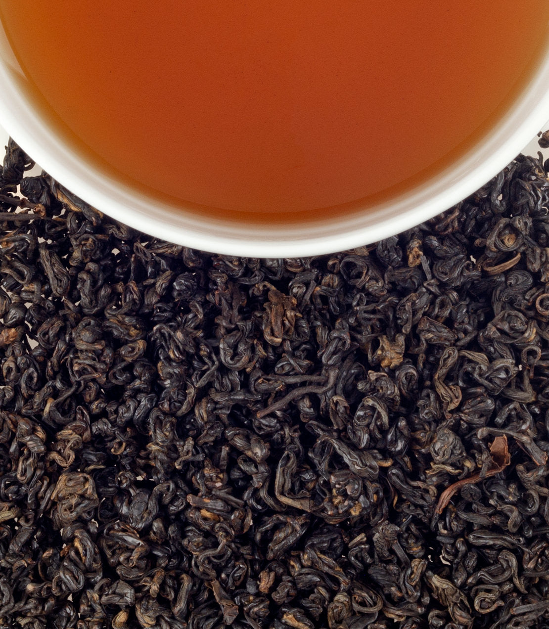 A cup of brewed Songluo Full tea above a bed of dried black tea leaves.