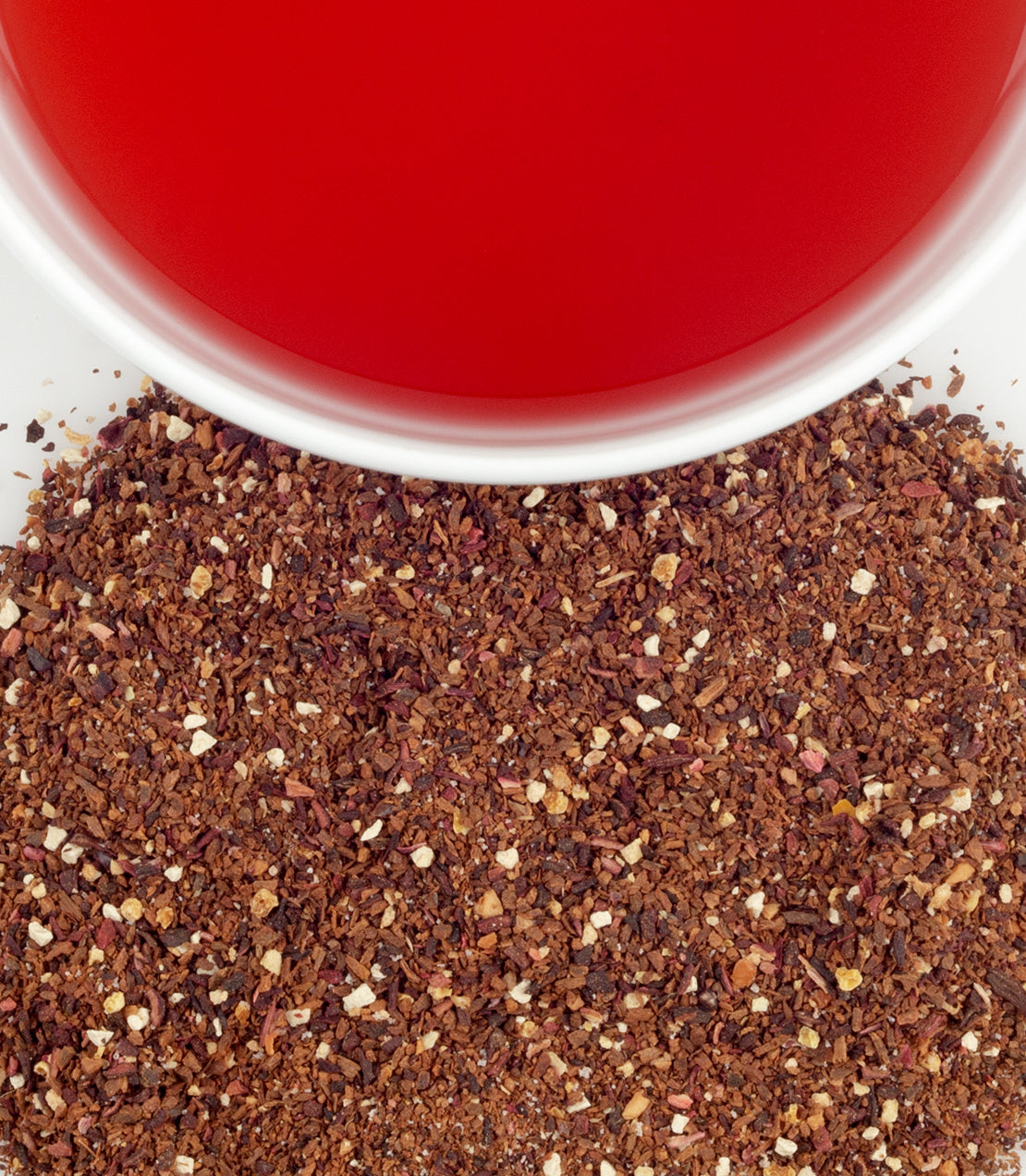 Close-up of spiced plum herbal tea leaves with a vibrant red tea in a white cup above.