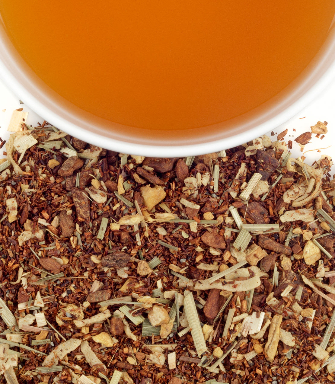 A cup of brewed Thai Rooibos tea above a pile of loose tea leaves and herbs, showcasing its rich color and texture.