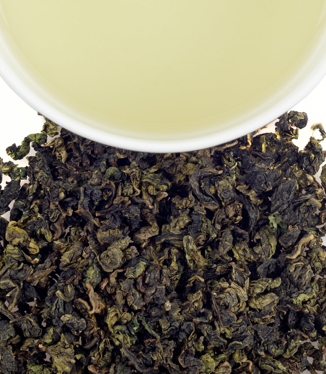 Ti Quan Yin Spring Floral oolong tea leaves beside a cup of pale green tea, showcasing its rich texture and color.