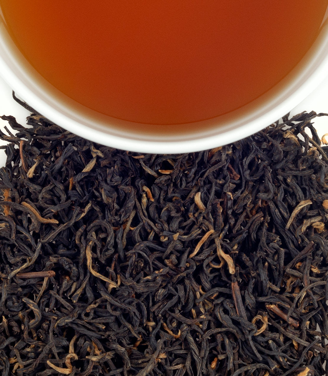 A close-up of Tippy Yunnan black tea leaves with a cup of brewed tea above, showcasing rich color and texture.